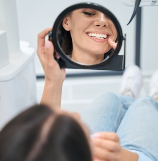 Dental patient looking in mirror and pointing to her smile