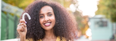 Smiling woman holding an Invisalign clear aligner