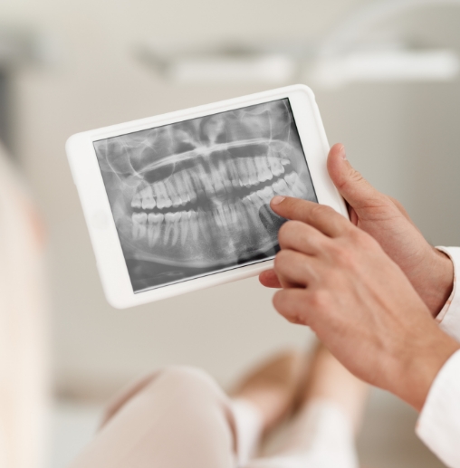 Dentist pointing to tablet screen showing x rays of teeth