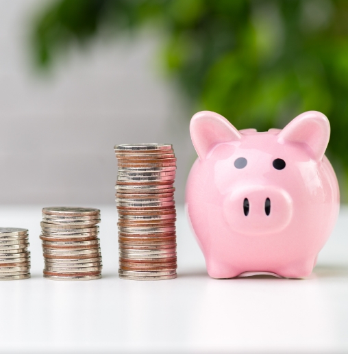 Pink piggy bank on table next to three stacks of coins