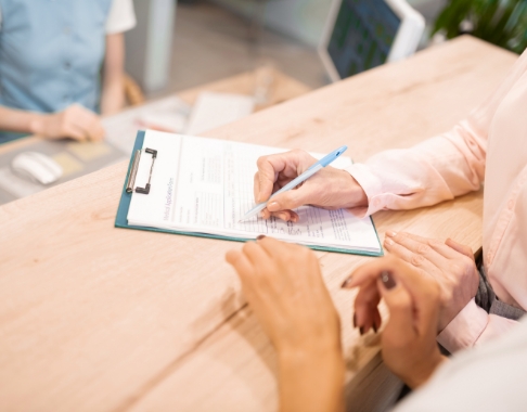 Person signing paper on clipboard at dental office front desk