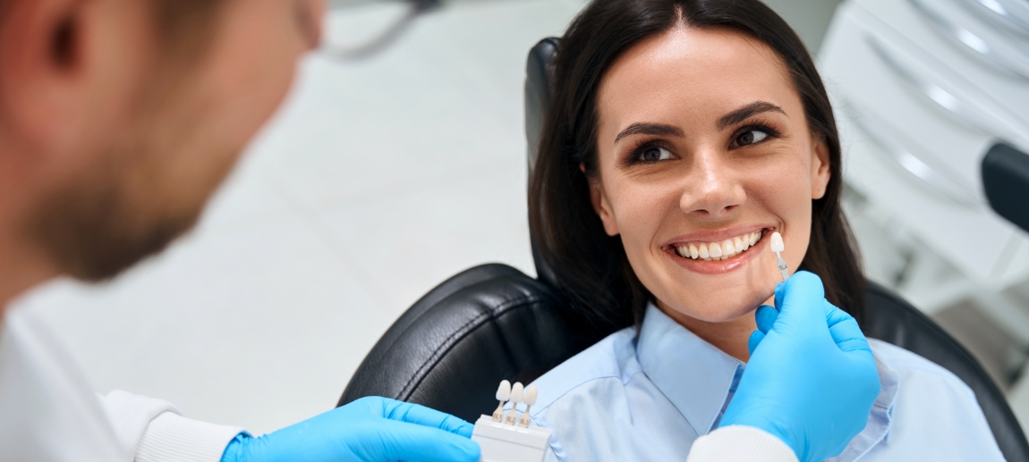 Dentist holding a veneer in front of a smiling patient