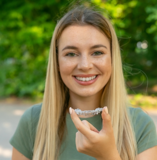 Smiling young woman holding an Invisalign clear aligner in Colorado Springs