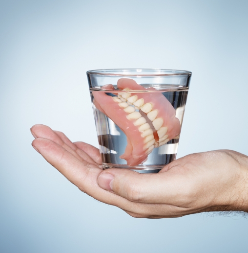 Hand holding a glass of water with dentures soaking in it