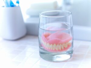 Dentures in glass of clear liquid on tiled countertop